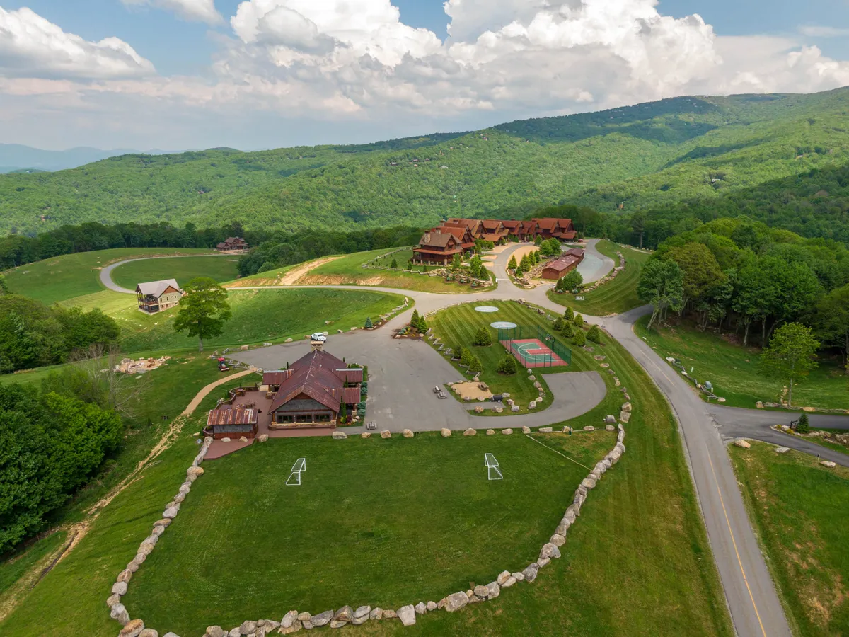 A spacious lodge with manicured lawns, a basketball court, walking paths, and a scenic mountain backdrop. The image conveys a sense of open space for outdoor sports and gatherings set within the natural beauty of the mountains.