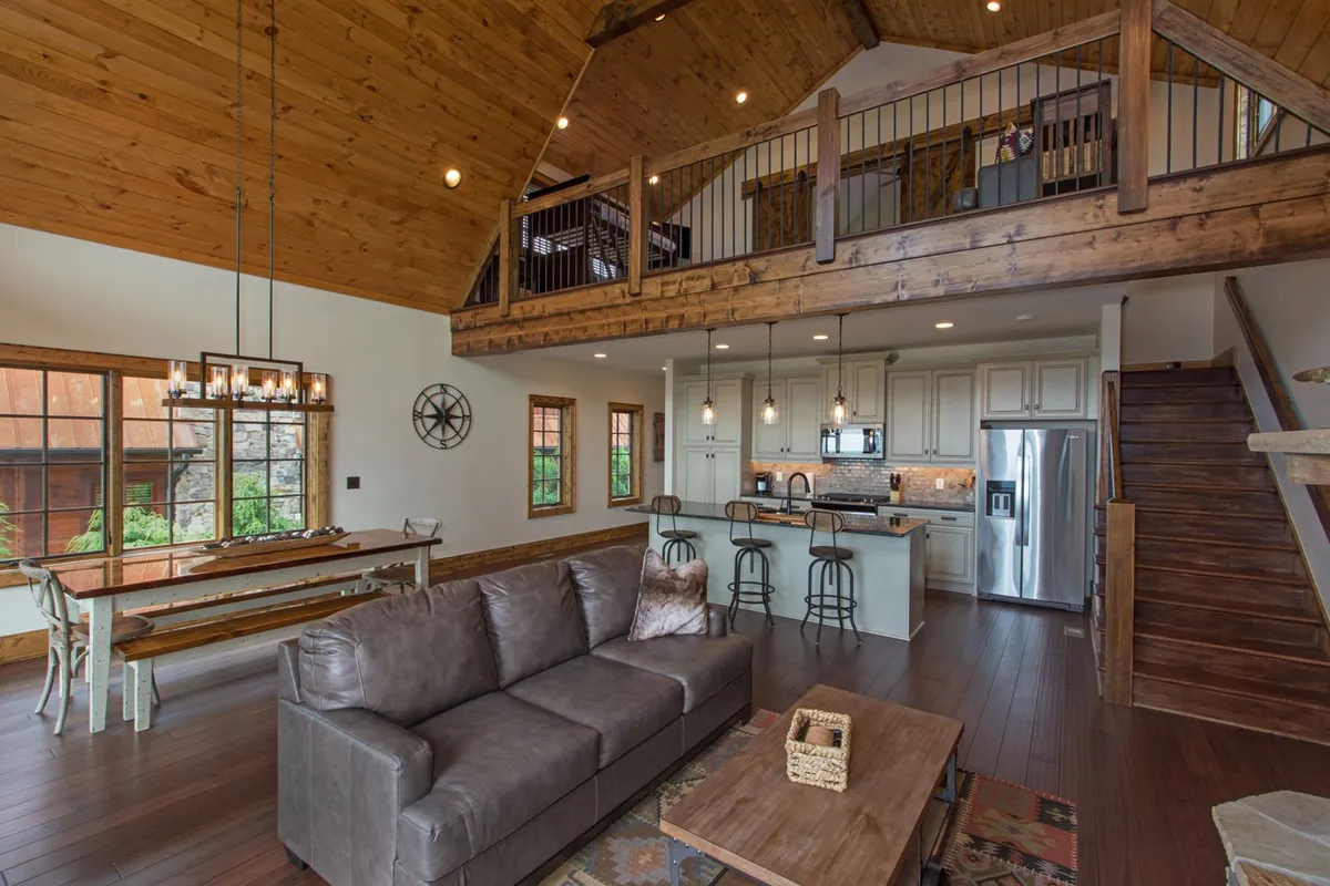This image provides a comprehensive view of the open-concept living area, including a spacious sofa, the dining table, kitchen island, staircase, and large windows that usher in natural light. It captures the core gathering space described in the section, with clear sightlines connecting the living, dining, and kitchen zones in one inviting space.