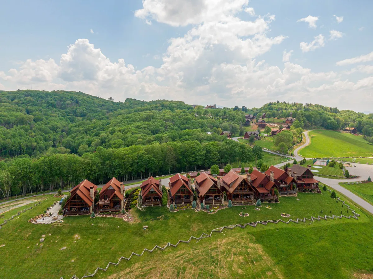 An exterior view of multiple wooden lodges nestled among lush greenery, with a curved pathway winding through the scene. The picnic and gathering areas suggest opportunities for outdoor activities, nature walks, and family get-togethers within the broader community environment.