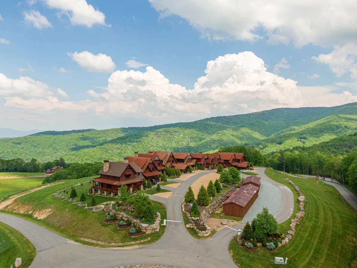This image features a tranquil scene of a mountain range behind a cluster of rustic cabins, surrounded by landscaped gardens and a winding driveway. The natural setting evokes a sense of adventure and togetherness, perfect for family gatherings or group activities.