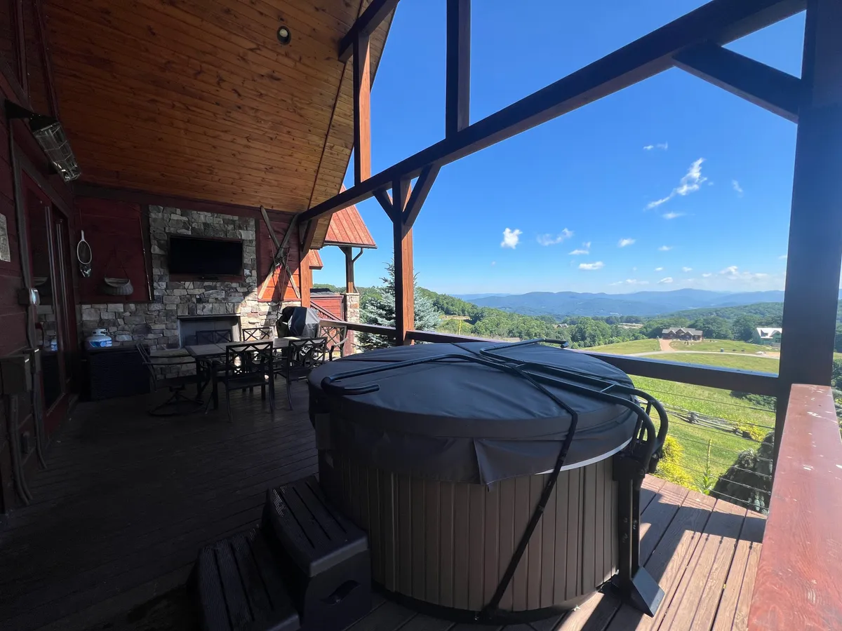 This exterior image shows a private hot tub and outdoor seating area overlooking majestic mountain views. A stone outdoor fireplace adds a touch of luxury, while the tranquil ambiance reflects relaxation after a day of excitement.