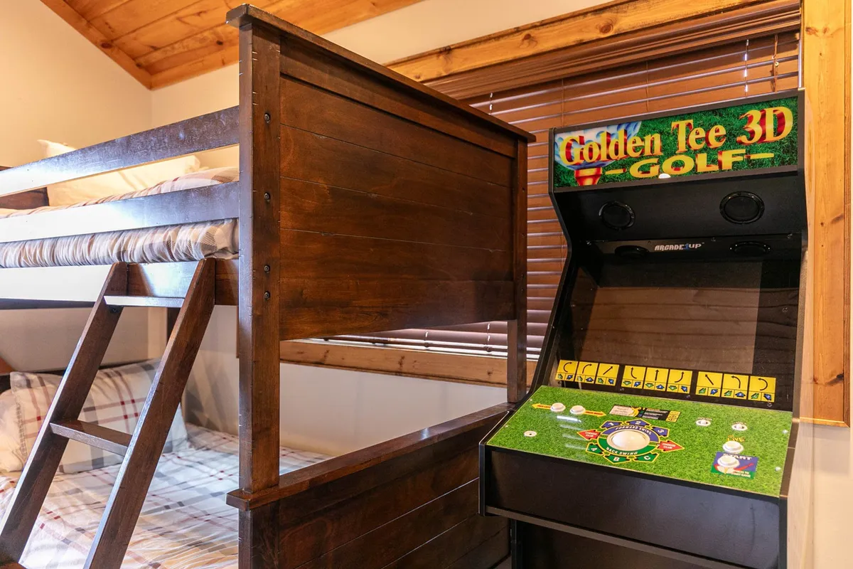 A playful loft space with a twin-over-twin bunk bed and a classic arcade game, perfect for kids or late-night game sessions. The decor is bright and fun, appealing to families and groups.