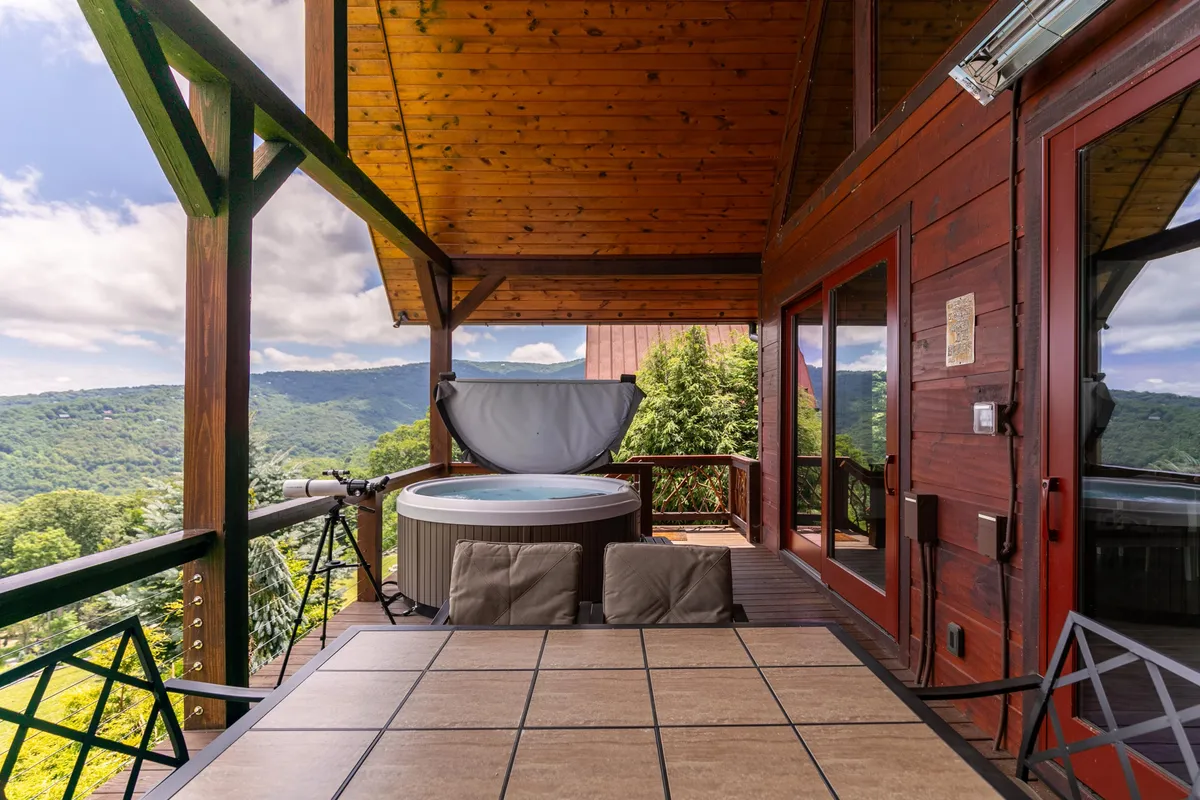 This image displays an inviting exterior deck featuring a hot tub, outdoor dining table, and expansive mountain views. The deck offers ample space for relaxing and socializing in a peaceful natural setting. This versatile outdoor area is perfect for guests who want to spend time with their pets while taking in the scenery.