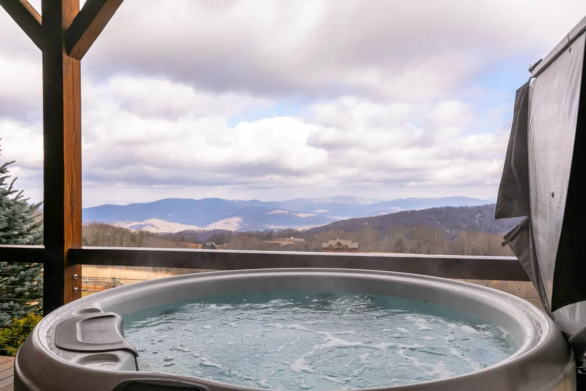 An exterior shot of a hot tub on the deck, framed by panoramic mountain views and a soft, cloudy sky. The setting suggests peaceful moments and opportunities for outdoor relaxation with pets, as well as space for exploration just beyond the deck.