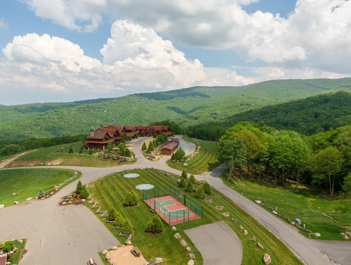 A serene community setting showcasing a lodge-style building, tennis courts, and lush, well-manicured lawns nestled within a mountainous landscape. The atmosphere is recreational and inviting, perfect for sports and relaxation.